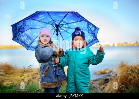 Bambina e ragazzo con ombrellone a giocare sotto la pioggia. Bambini a giocare all'aperto da tempo piovoso in autunno. In autunno il divertimento per i bambini. Il Toddler kid in una giacca impermeabile Foto Stock