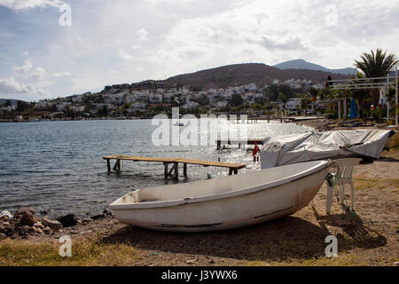 Vista della spiaggia vuota, piccolo molo e white piccola barca al villaggio di Turkbuku nella penisola di Bodrum, in autunno. L'immagine mostra anche come le crisi del turismo effec Foto Stock