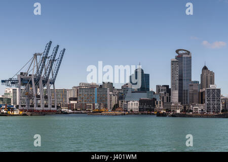 Auckland, Nuova Zelanda - 3 Marzo 2017: fila di container gru a porto commerciale con parte della skyline della città in indietro sotto il cielo blu e dietro greeni Foto Stock