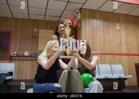 Tre giovani donne con un trofeo in una pista da bowling. Foto Stock