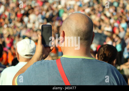 Uomo a scattare foto in una folla sul suo telefono cellulare Foto Stock