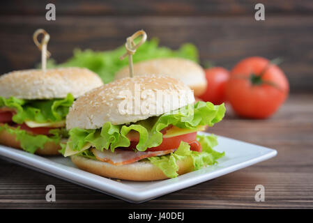 Burger con pancetta, pomodoro e formaggio sulla piastra su un tavolo di legno Foto Stock