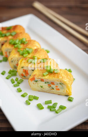 Dashimaki tamago - giapponese frittata arrotolata su piastra bianca su sfondo di legno Foto Stock