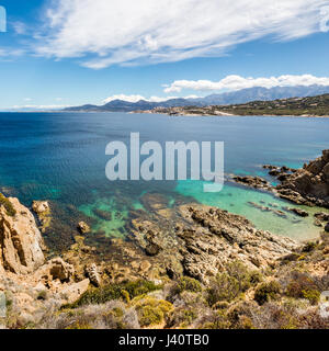 Traslucido acque turchesi del mar mediterraneo e la costa rocciosa a Revellata nella regione della Balagne in Corsica con la cittadella di Calvi a distanza Foto Stock