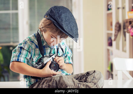 Carino piccolo ragazzo in abito retrò holding vecchia fotocamera a pellicola. Foto Stock