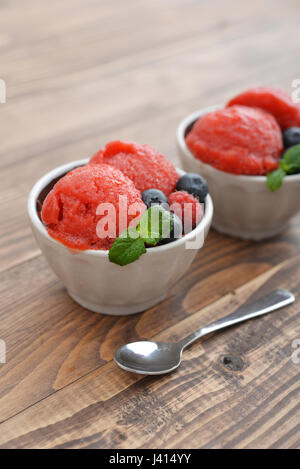 Frutta sorbetto di fragole con lampone, mirtillo e menta in una ciotola su sfondo di legno Foto Stock