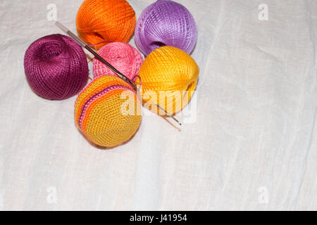 A crochet in corso e colorato filo di cotone le sfere sulla biancheria da letto bianca con uno sfondo con spazio di copia Foto Stock