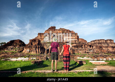 Coppia giovane in rosso vestiti con fotocamera foto guardando antichi rovinato Wat Mahathat in Ayutthaya, Thailandia Foto Stock