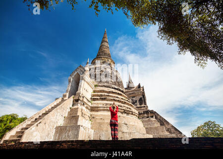 Tourist donna in costume rosso pregando vicino antico stupa in rovina in Ayutthaya parco storico, Thailandia Foto Stock