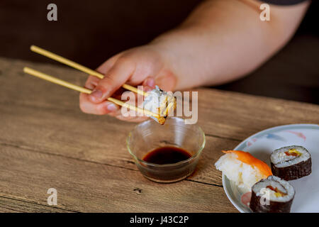 Impostare il sushi set. Mano con bacchette per sushi. Futomaki sushi roll con salmone, avocado e nori Foto Stock