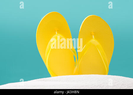 Giallo flip flop sulla spiaggia contro sfondo blu. Foto Stock