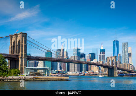 Luminoso panoramico vista Diurna del Ponte di Brooklyn con la parte inferiore della skyline di Manhattan in tutta l'East River sotto il cielo blu chiaro Foto Stock