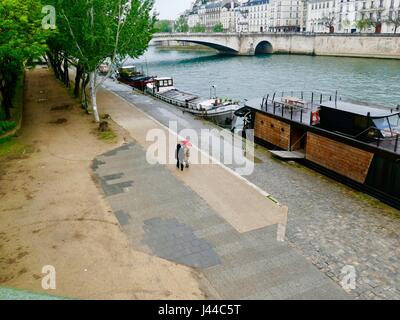 Matura in tute impermeabili con ombrellone rosso, passeggiate lungo il Fiume Senna e barche sotto la pioggia. Quai de la Tournelle, Parigi, Francia. Foto Stock