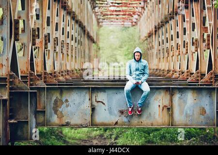 Triste Uomo con telefono cellulare sul abbandonato ponte arrugginito. Concetto di tristezza e solitudine, collegamento e altro ancora. Foto Stock