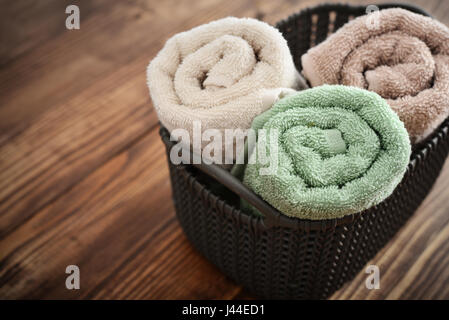 Asciugamani da bagno di colori diversi nel cesto in vimini su sfondo di legno Foto Stock