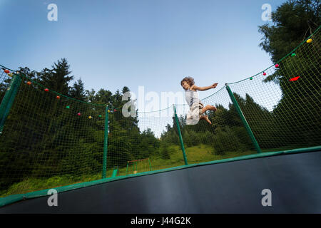 Carino ragazzo gode di salto e rimbalzare sul trampolino oudoors. Foto Stock