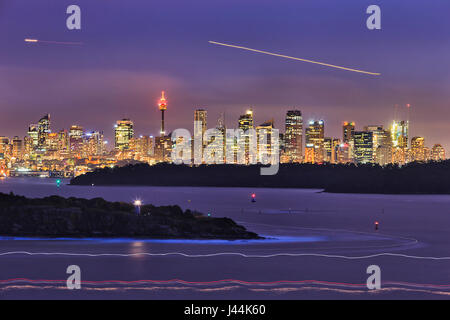 Cityline di Sydney CBD oltre il porto di acque sfocata e arenaria shore capi al tramonto quando la città è illuminato. Foto Stock