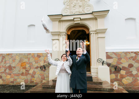 Sposa giovane rilasciando colombe bianche quando si lascia la chiesa dopo la loro cerimonia di nozze Foto Stock