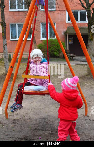 Due sorelle Vivid Riproduci sul swing sul parco giochi nella giornata di primavera Foto Stock