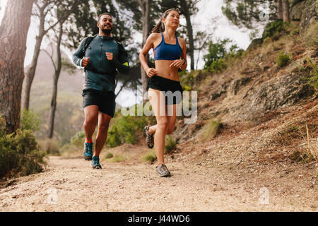 Montare la coppia giovane in esecuzione sul sentiero di montagna in mattina. Giovane uomo e donna jogging sul percorso del paese. Foto Stock