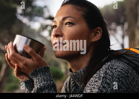 Close up side shot femminile di escursionista in appoggio all'aperto con un caffè e guardare lontano. Donna asiatica avente il caffè. Foto Stock