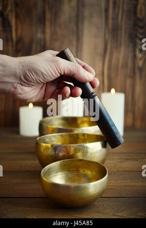 Maschio lato riproduzione su artigianali tibetani SINGING BOWLS su sfondo di legno Foto Stock