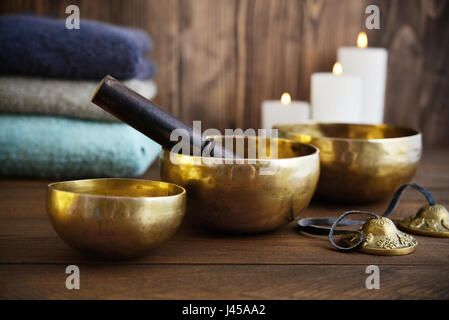 Il Tibetano handcrafted SINGING BOWLS con asciugamani e candele su sfondo di legno Foto Stock