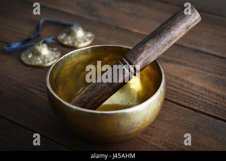 Il Tibetano handcrafted Singing Bowl con bastone su sfondo di legno Foto Stock