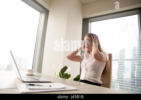 Sorpreso imprenditrice seduta con testa in mani Foto Stock