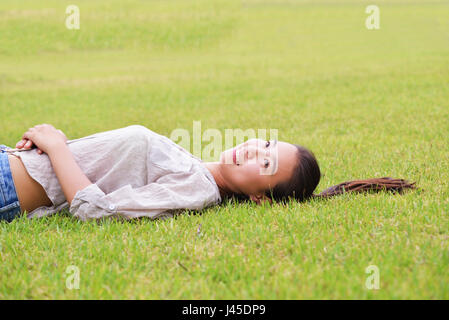 Felice ragazza asiatica giacente in erba Foto Stock