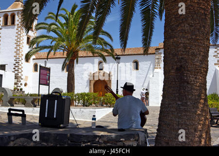 Uomo di suonare una chitarra in ombra, di fronte alla chiesa di Santa Maria de Betancuria, sull'isola spagnola di Fuerteventura, Spagna Foto Stock