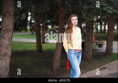 Una bella ragazza con lunghi capelli rossi, passeggiate attraverso il parco e sorrisi ritratto all'aria aperta Foto Stock