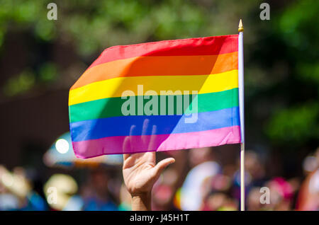 Una mano di supporto sventolare dietro una bandiera arcobaleno battenti sul margine di un estate Gay Pride Parade Foto Stock