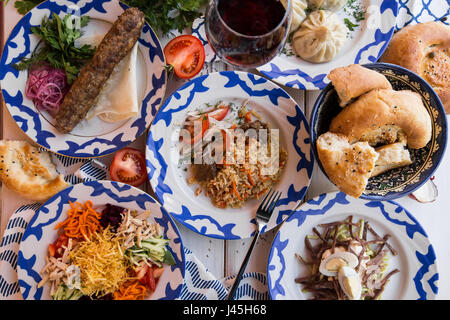 Tradizionale cena uzbeka. Pilaf, manta, kebab, il pane sulla tavola con verdure Foto Stock