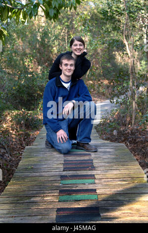 Sorella e fratello pausa nel loro camminare attraverso il sud arkansas arboretum in El Dorado, Arkansas. fratello si inginocchia sulla passerella di legno e sorella l Foto Stock