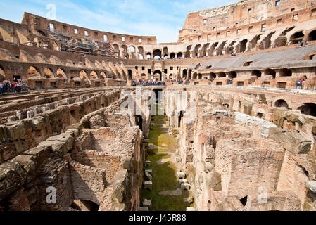 Un ampio angolo di vista interna dell'anfiteatro all'interno del Colosseo con i turisti i visitatori in una giornata di sole con cielo blu preso dal livello del suolo. Foto Stock