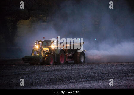 Imprenditore lavorare fino a tarda notte spandimento di calce dal suo le luci del trattore Foto Stock