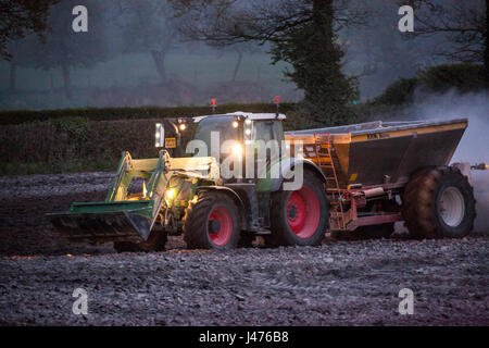 Imprenditore lavorare fino a tarda notte spandimento di calce dal suo le luci del trattore Foto Stock