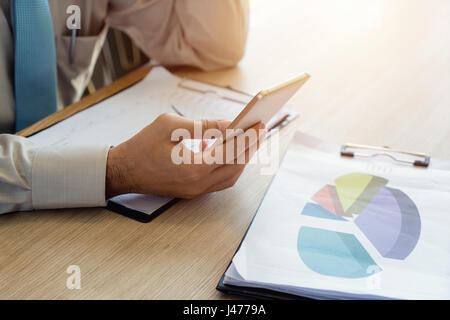 Close-up di senior business uomo che lavora nel bar interno e tenendo lo smartphone e guardando lo schermo con diagrammi di business nella caffetteria o ufficio. Office Foto Stock