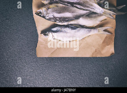 Tutto il pesce essiccati in roach bilance giacente su carta marrone, uno spazio vuoto al fondo tonificante vintage Foto Stock