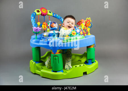 Carino multi-razziale asian caucasian sorridente baby boy in giallo bib giocando nel ponticello colorati contro un sfondo grigio Foto Stock