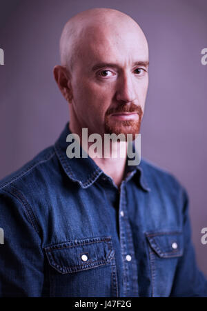 Ritratto di un triste e arrabbiato cerca uomo calvo con un pizzetto rosso indossando un blu denim chambray camicia da cowboy Foto Stock