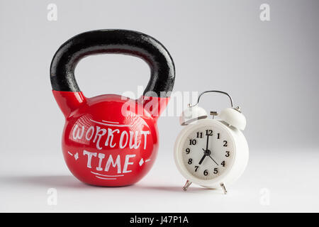 Red kettlebell con tempo di allenamento caratteri scritti su di esso e la tradizionale sveglia isolato su bianco con copia spazio. Il tempo di lavorare fuori, vita sana Foto Stock