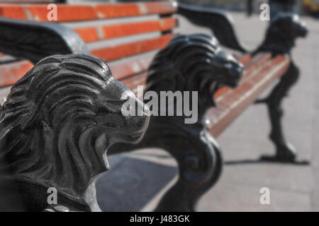 Una panchina nel parco con ghisa gambe in forma di una testa di leone Foto Stock