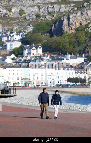 Un maschio e femmina giovane a piedi lungo la passeggiata costiera a Llandudno, il Galles del Nord con il Great Orme rock formazione e alberghi a distanza Foto Stock