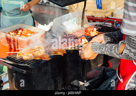 CHIANG MAI, Thailandia - 21 agosto: tailandese uomo cuochi carne sul mangal al mercato di domenica (walking street) il 21 agosto 2016 a Chiang Mai, Thailandia. Foto Stock