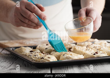 Baker mettendo mantecato uovo spalmare sulla parte superiore di appena arrotolato mini croissant appena prima della loro cottura Foto Stock