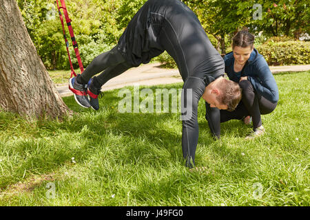 L'uomo sling allenamento con personal trainer in estate presso il parco Foto Stock