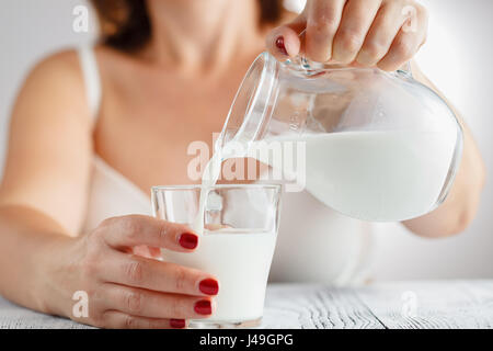 Mano Womans versando il latte da una caraffa in un bicchiere Foto Stock