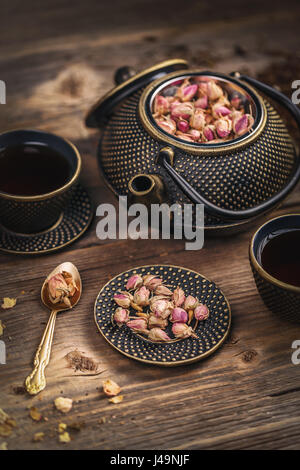 Asciutto boccioli di rosa, una tazza di tè caldo e teiera in ferro su sfondo di legno Foto Stock